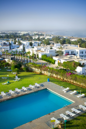 Weiße Hotelanlage mit schönem Pool und viel Grün in Agadir. Im Hintergrund die Bucht von Agadir mit ihrem weitläufigen Sandstrand